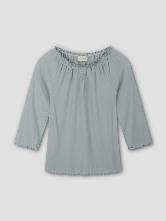 The Cotton Flounce 3/4 Sleeve - Baby Blue by Deiji Studios is a soft, fitted women's top with a scoop neck and ruffle details on the neckline and sleeves, shown against a plain white background.