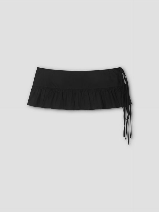 The Flounce Belt is a black mini skirt featuring a ruffled hem and side tie details, shown against a plain light grey background.