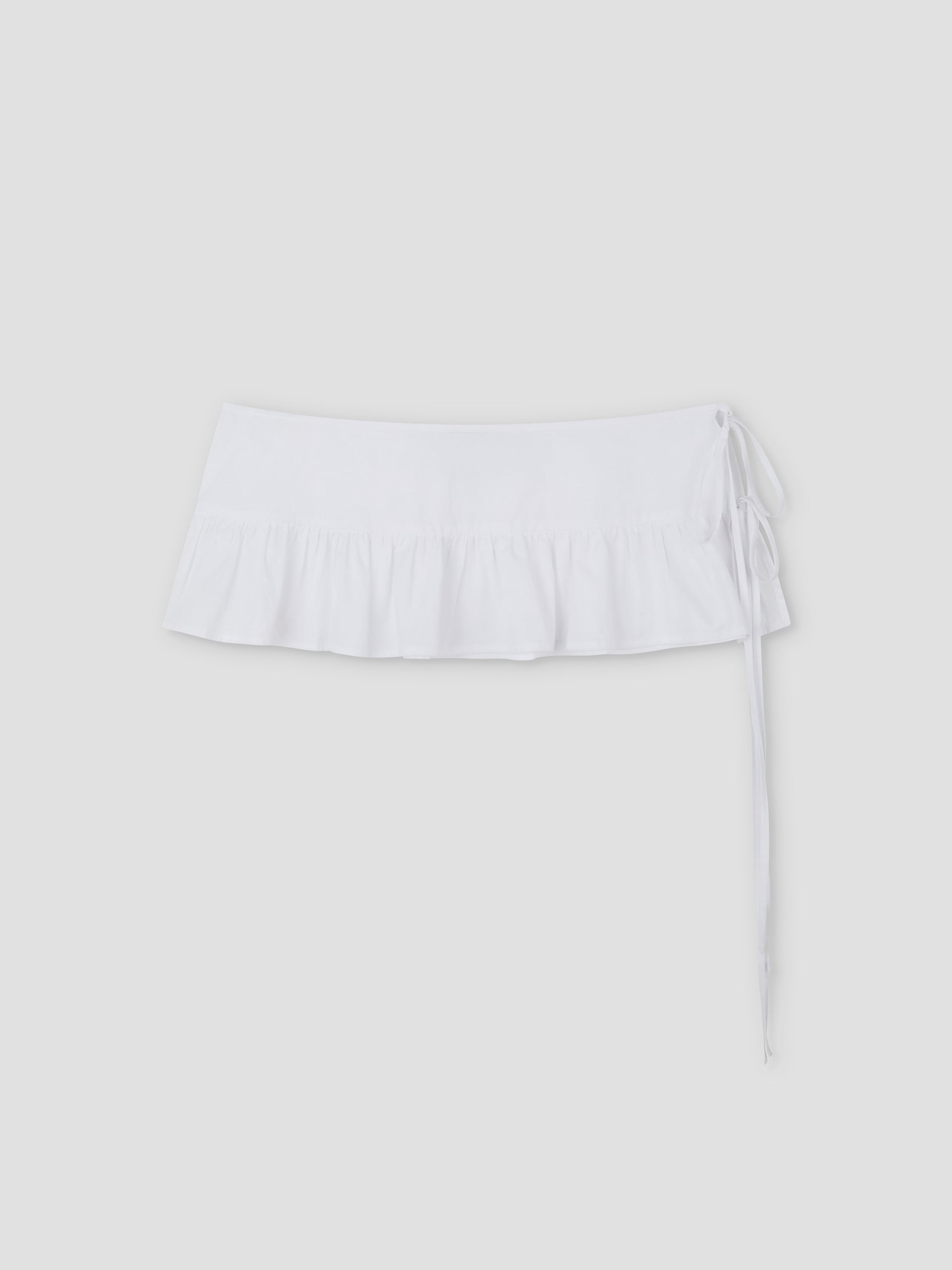 The Flounce Belt is a white mini skirt featuring a ruffled hem and side tie, shown against a plain light gray background.