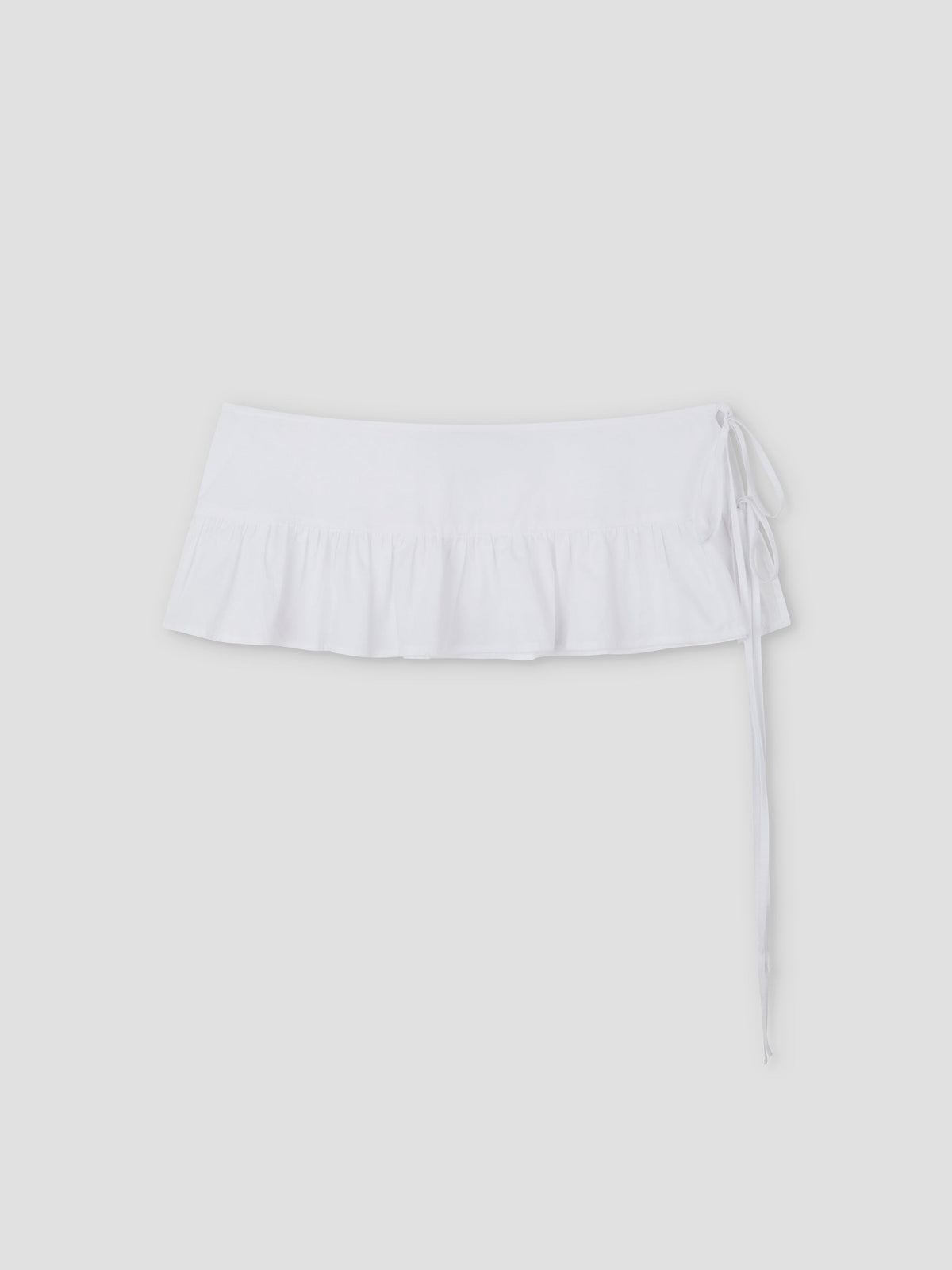 The Flounce Belt is a white mini skirt featuring a ruffled hem and side tie, shown against a plain light gray background.