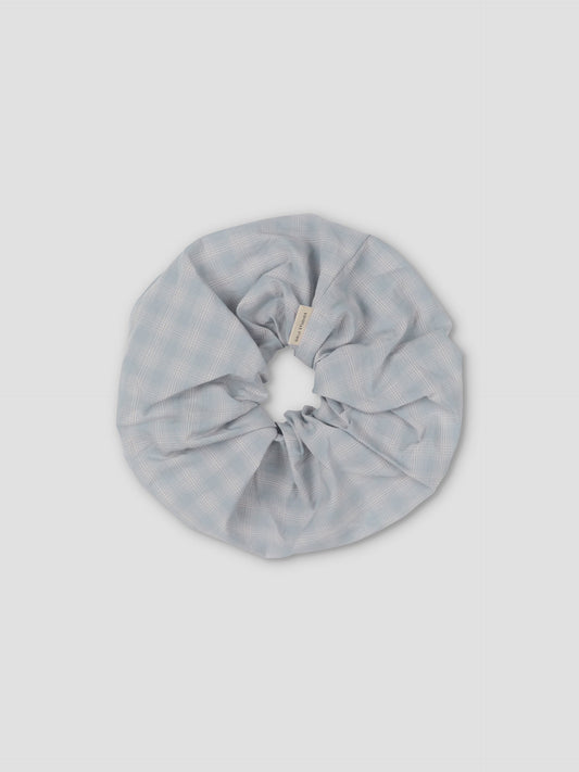 The Scrunchie is a large, light blue hair accessory with a subtle checkered pattern, shown on a plain light gray background.