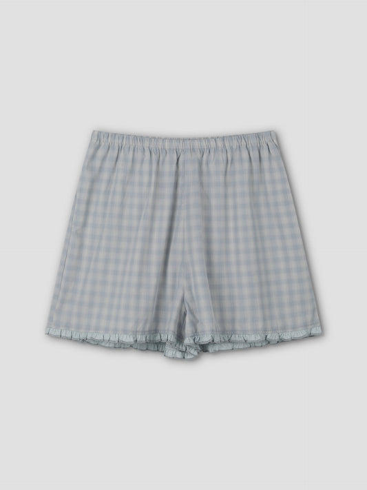 The Simple Short - Blue Check features a light blue and white check pattern, relaxed fit, elastic waistband, and subtle ruffle trim at the hem, shown on a plain light background.