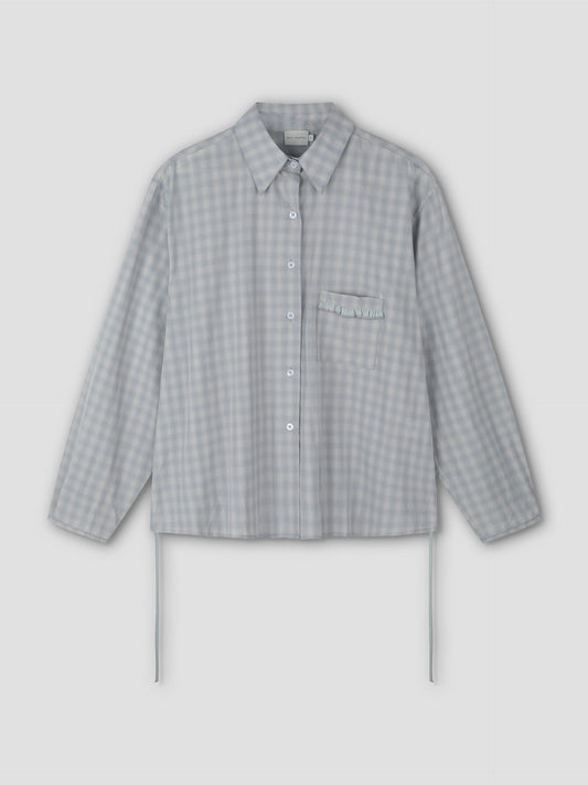 The Day Shirt - Blue Check features a light blue and white gingham pattern, boxy fit, long sleeves, collar, chest pocket with ruffle detail, and side ties. Shown as a button-up shirt on a plain light background.