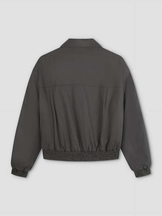 The Shirring Jacket - Slate features a dark gray color, long sleeves, collar, elastic waistband and cuffs, displayed from the back against a plain light background.