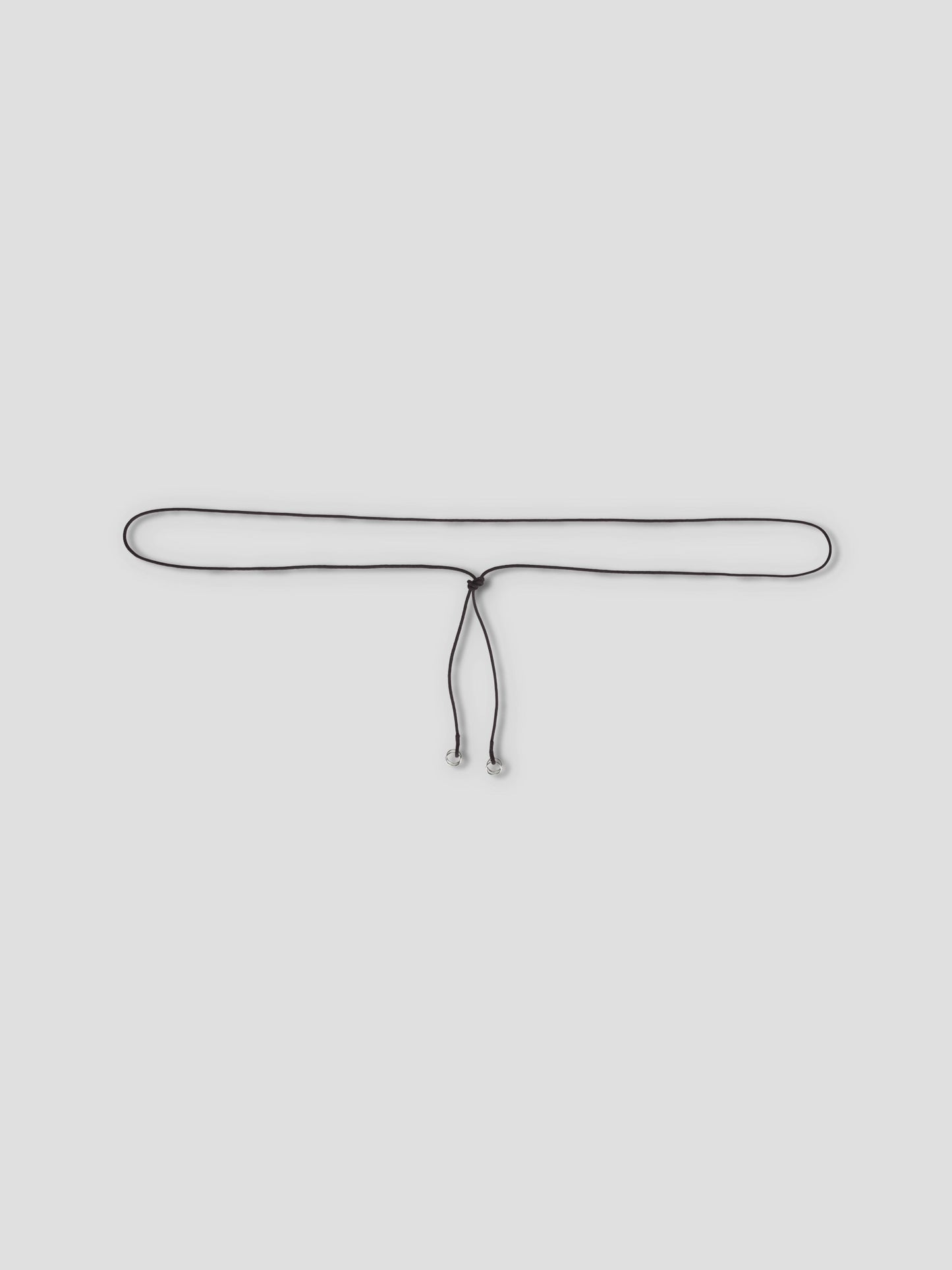 The Multi Ring Belt, a slim black accessory with metallic tips, is tied in a loose knot and showcased against a plain light grey background.
