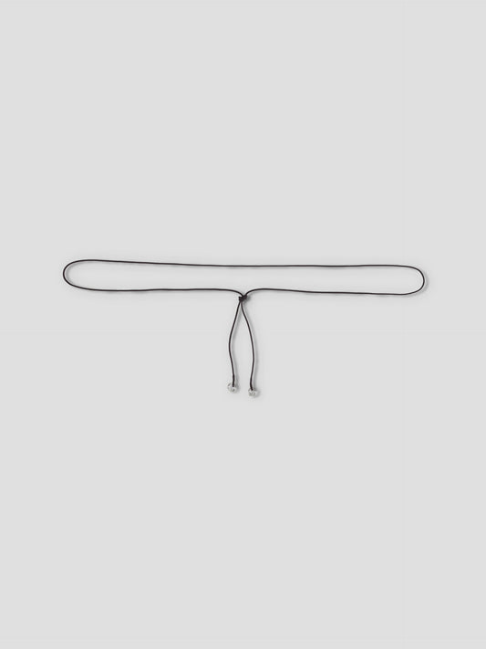 The Multi Ring Belt, a slim black accessory with metallic tips, is tied in a loose knot and showcased against a plain light grey background.