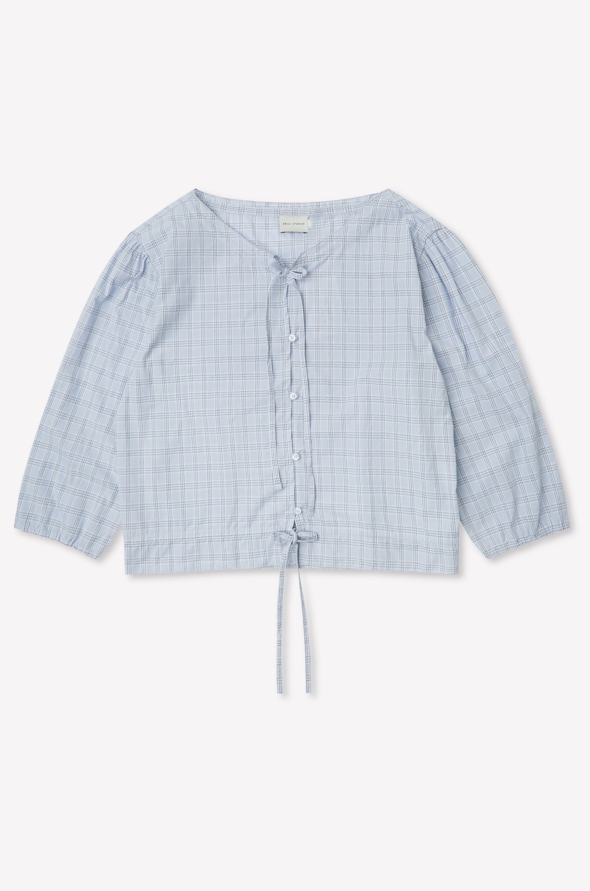 The Corded Top - Powder Check features a light blue, long sleeve design with a subtle check pattern, button-up front, V-neckline, drawstring waist, and slightly puffed sleeves. Inspired by Deiji Studios. Displayed flat on a white background.