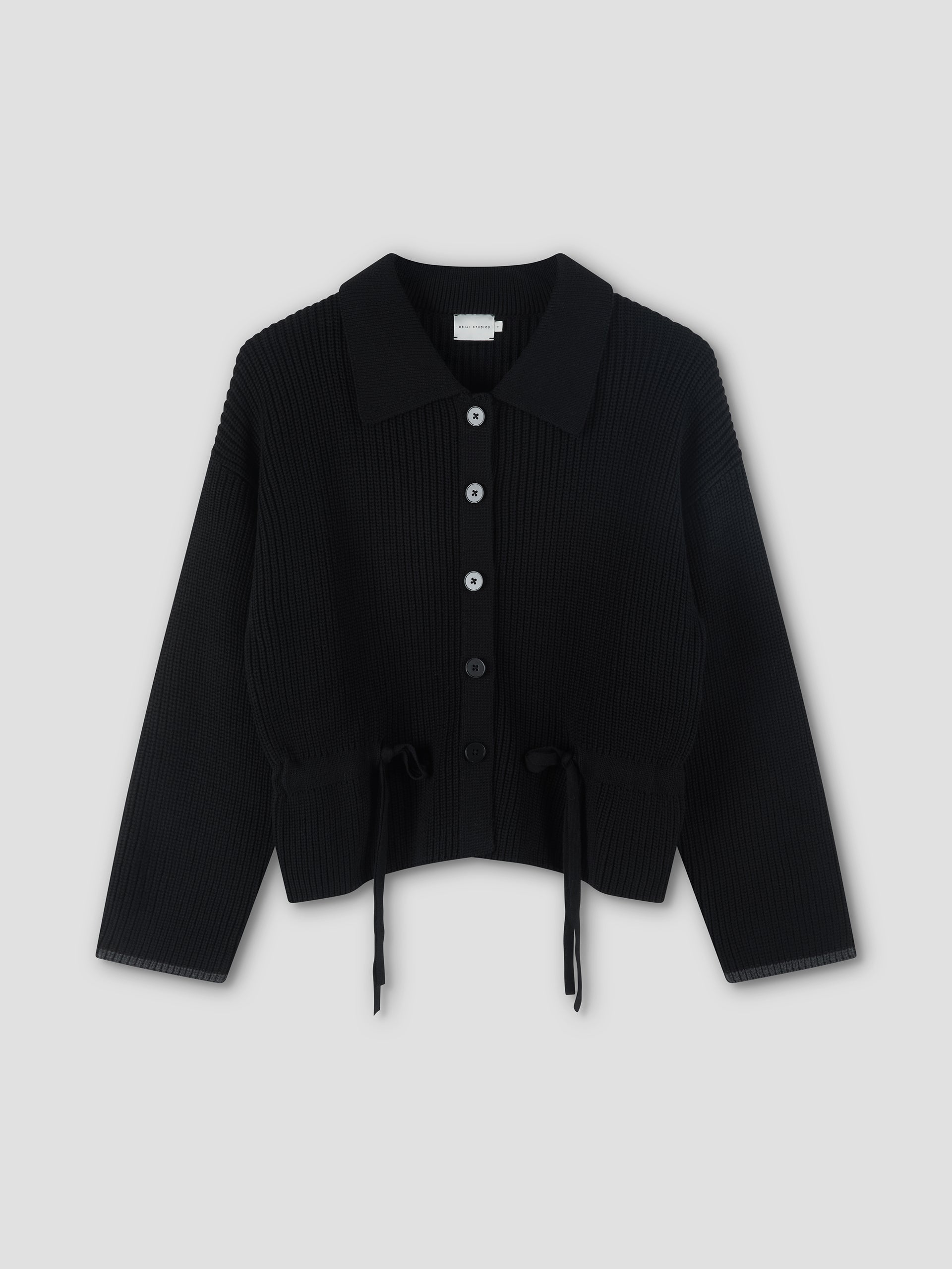The Tie Side Cardigan - Black by Deiji Studios features long sleeves, a collared neckline, button-down front, and waist drawstrings for a chic tie-side look, shown against a light gray background.