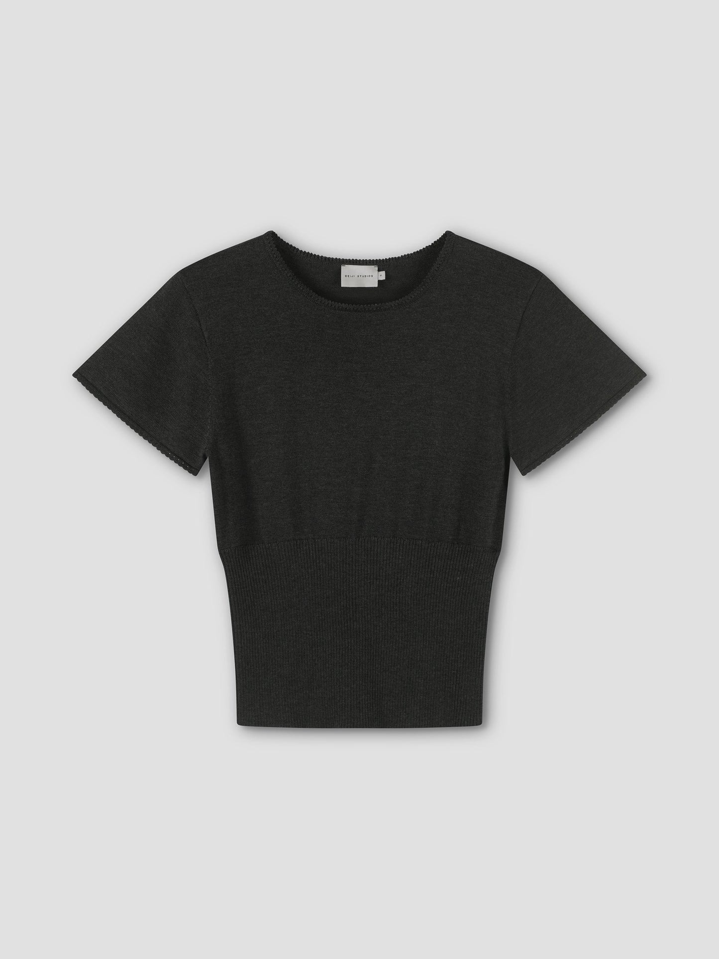 The Trim Knit Tee is a plain black short-sleeve knit top with a round neckline and fitted waist, shown on a light grey background.