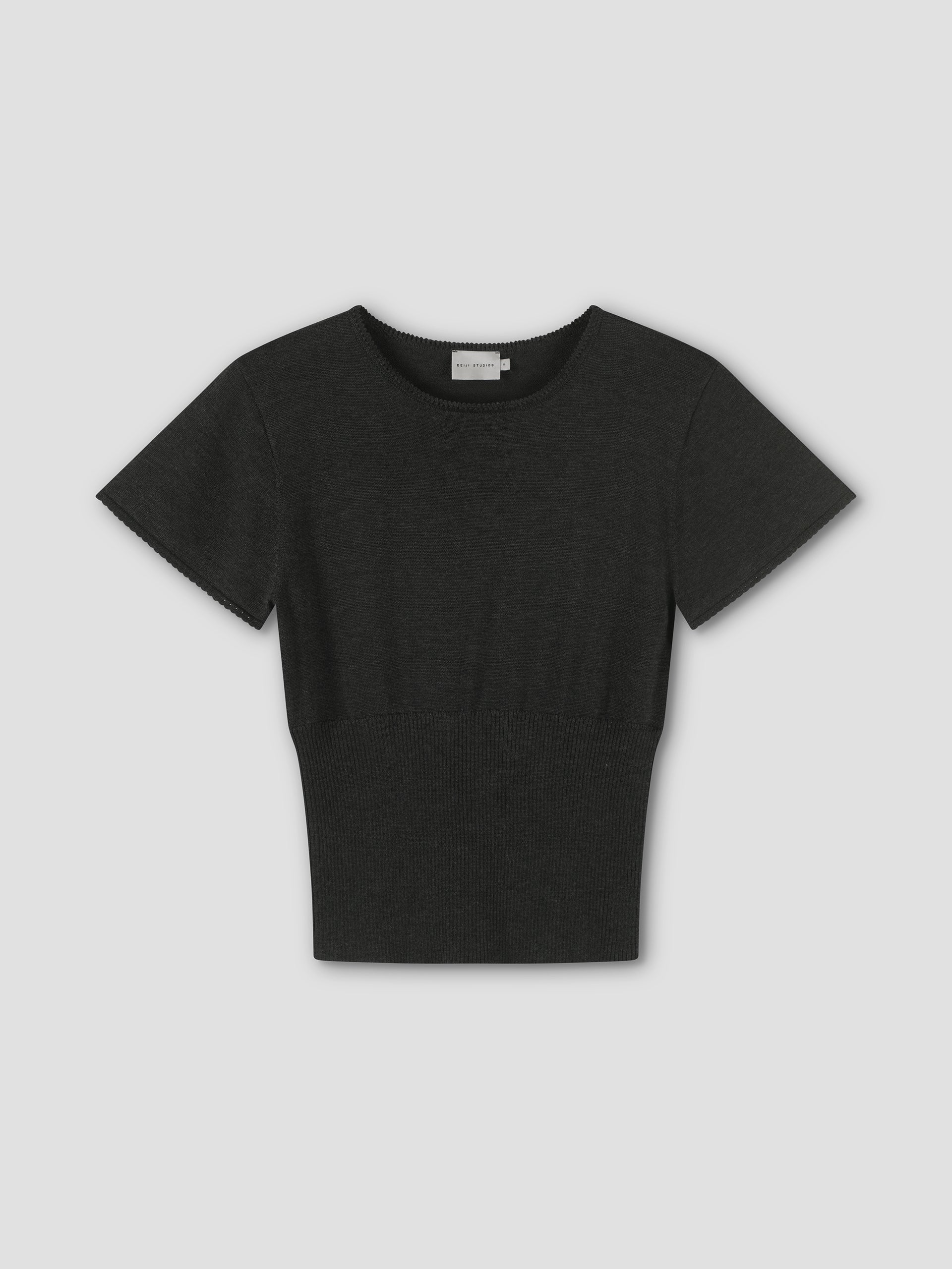 The Trim Knit Tee is a plain black short-sleeve knit top with a round neckline and fitted waist, shown on a light grey background.