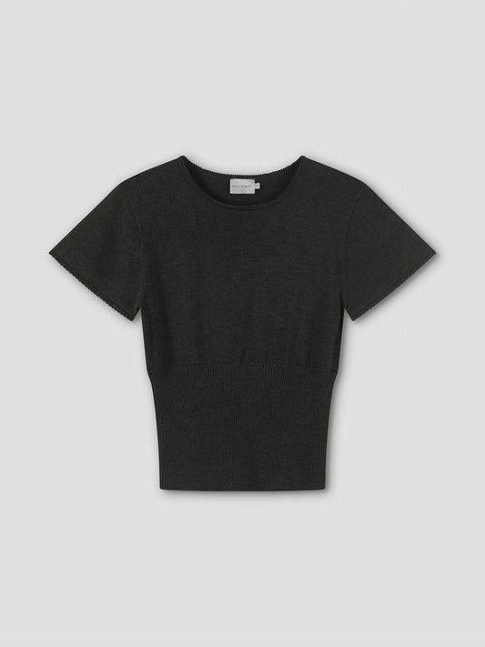 The Trim Knit Tee is a plain black short-sleeve knit top with a round neckline and fitted waist, shown on a light grey background.