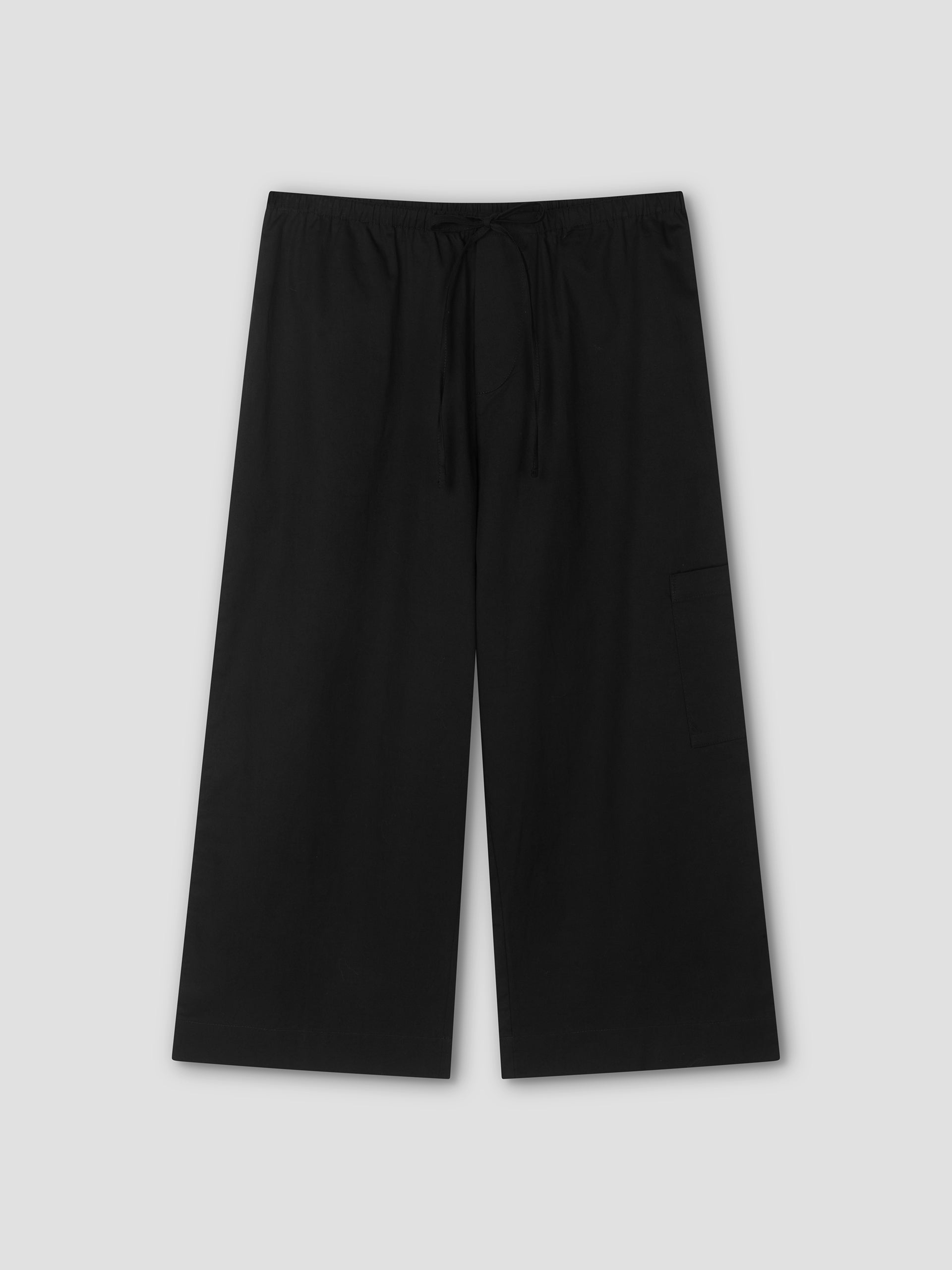 The Mid Pocket Short - Black by Deiji Studios features a relaxed, wide-leg fit with an elastic waistband, drawstring, and a visible right-side pocket. Displayed flat on a light gray background, these shorts evoke a comfortable 3/4 length style.