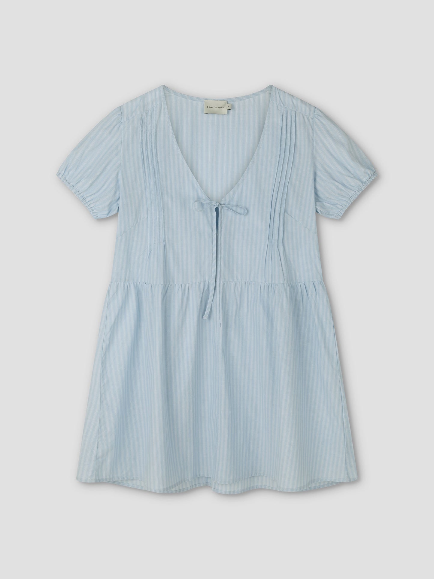 The V Pleat Dress - Lake Blue Stripe from Deiji Studios is a lightweight mini dress with short sleeves, thin vertical white stripes, a tie V-neckline, gathered waist, and v pleat accents, shown on a flat light background.