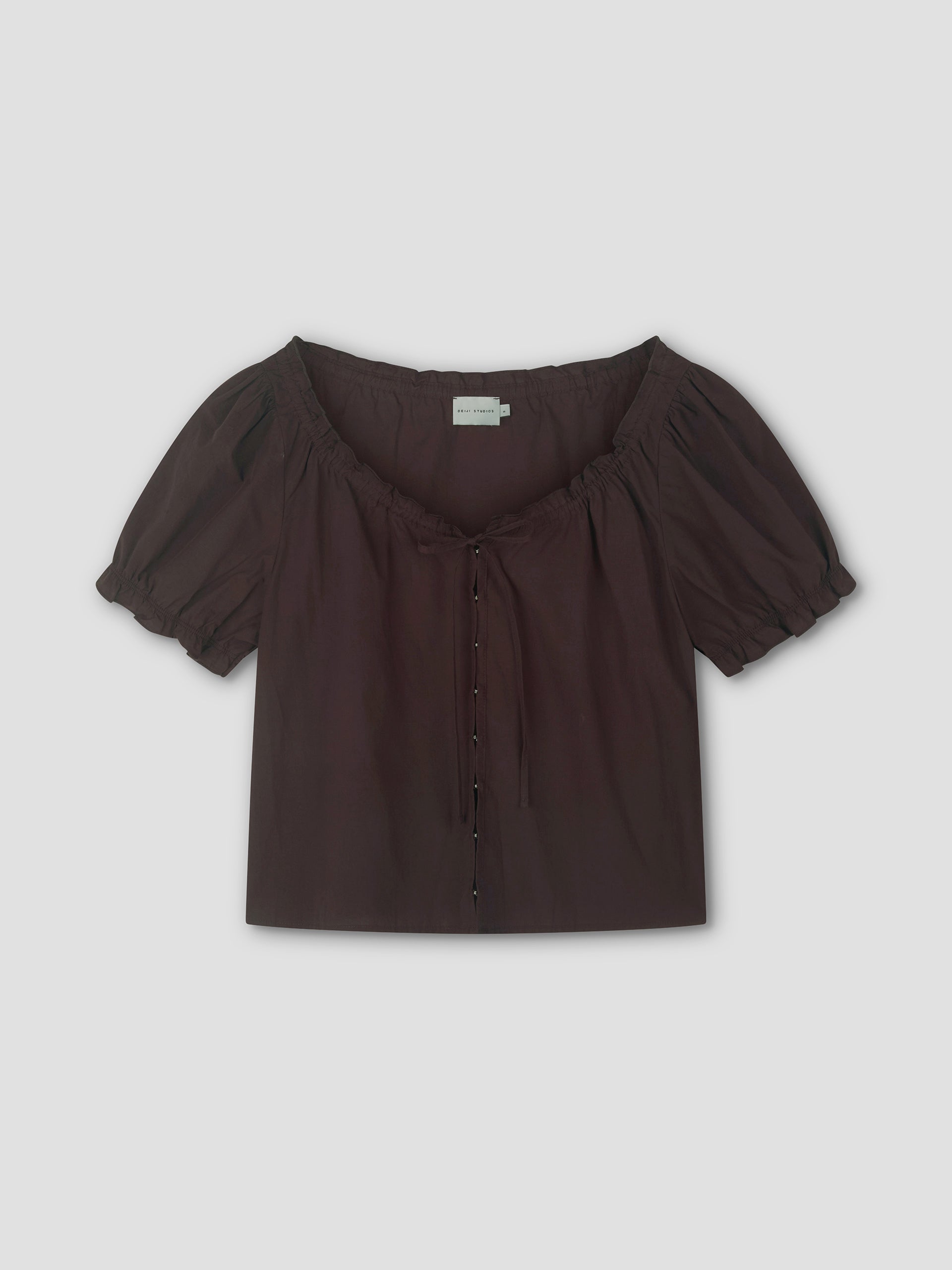 The Close Shirt - Sepia by Deiji Studios is a short-sleeved, dark brown blouse featuring a square neckline, puff sleeves with gathers, a drawstring neckline tie, and button-down front, shown on a plain light background.