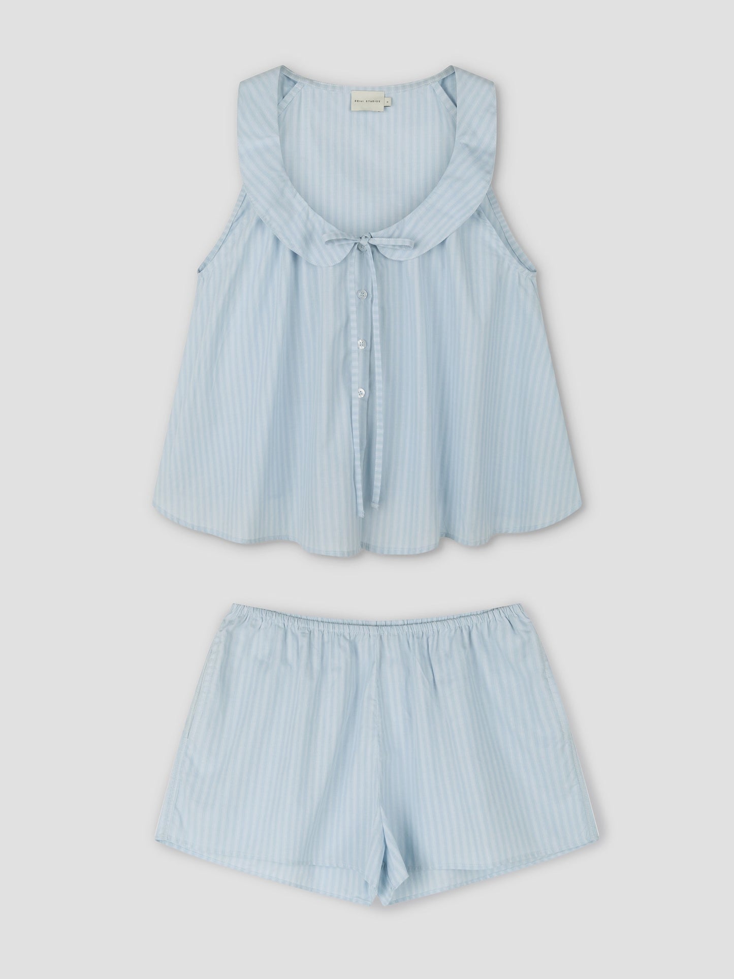 The Round Collar Set - Lake Blue Stripe is a sleeveless pajama set with white and blue stripes, round collar, front buttons, a bow detail, and loose-fit matching shorts. Inspired by Deiji Studios with soft, lightweight fabric.