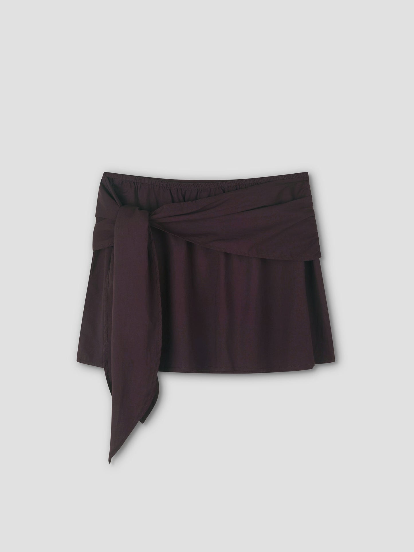 The Belted Skirt - Wine from Deiji Studios is a short, dark brown skirt with a wide matching fabric tie belt knotted at the front, shown against a plain light grey background.