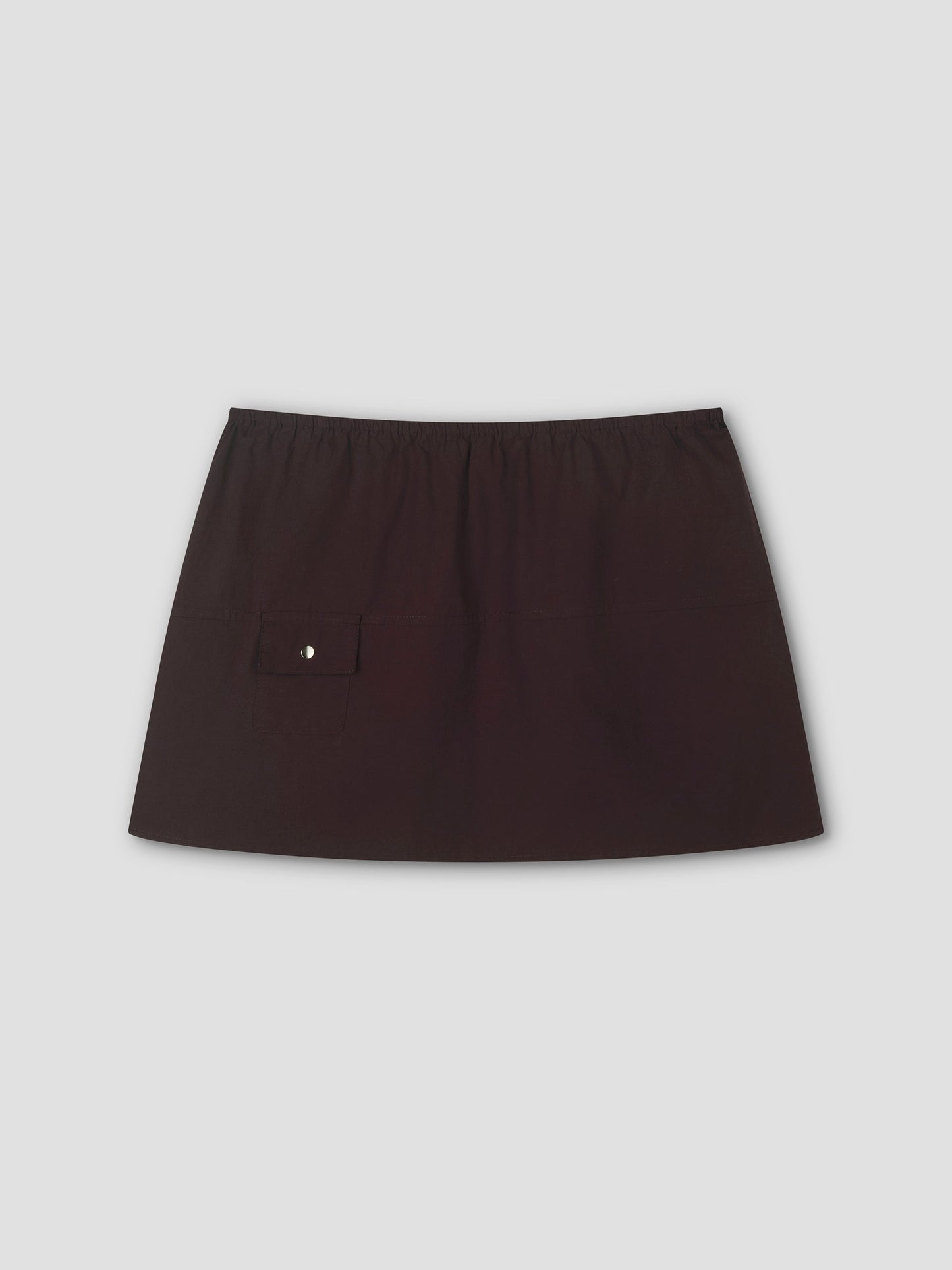 The Pocket Skirt - Sepia features an elastic waistband and a small buttoned flap pocket on the left, true to Deiji Studios style. This chic black mini skirt is displayed against a plain light gray background, perfect for any occasion.
