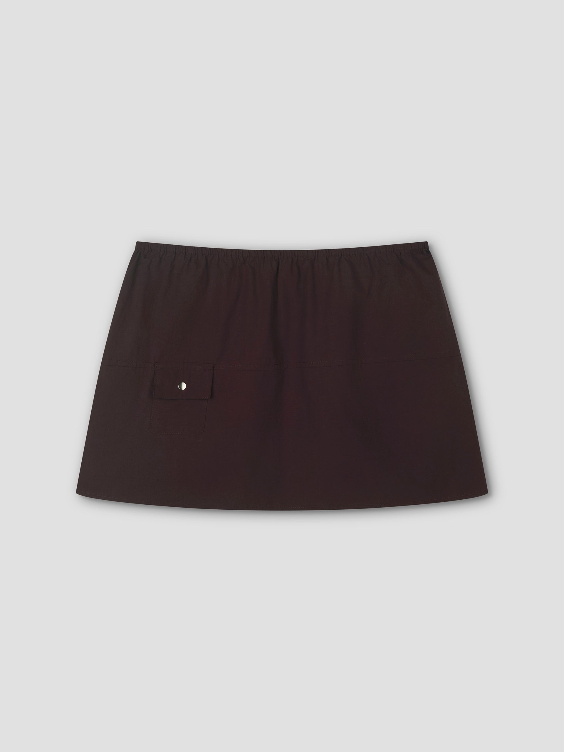 The Pocket Skirt - Sepia features an elastic waistband and a small buttoned flap pocket on the left, true to Deiji Studios style. This chic black mini skirt is displayed against a plain light gray background, perfect for any occasion.