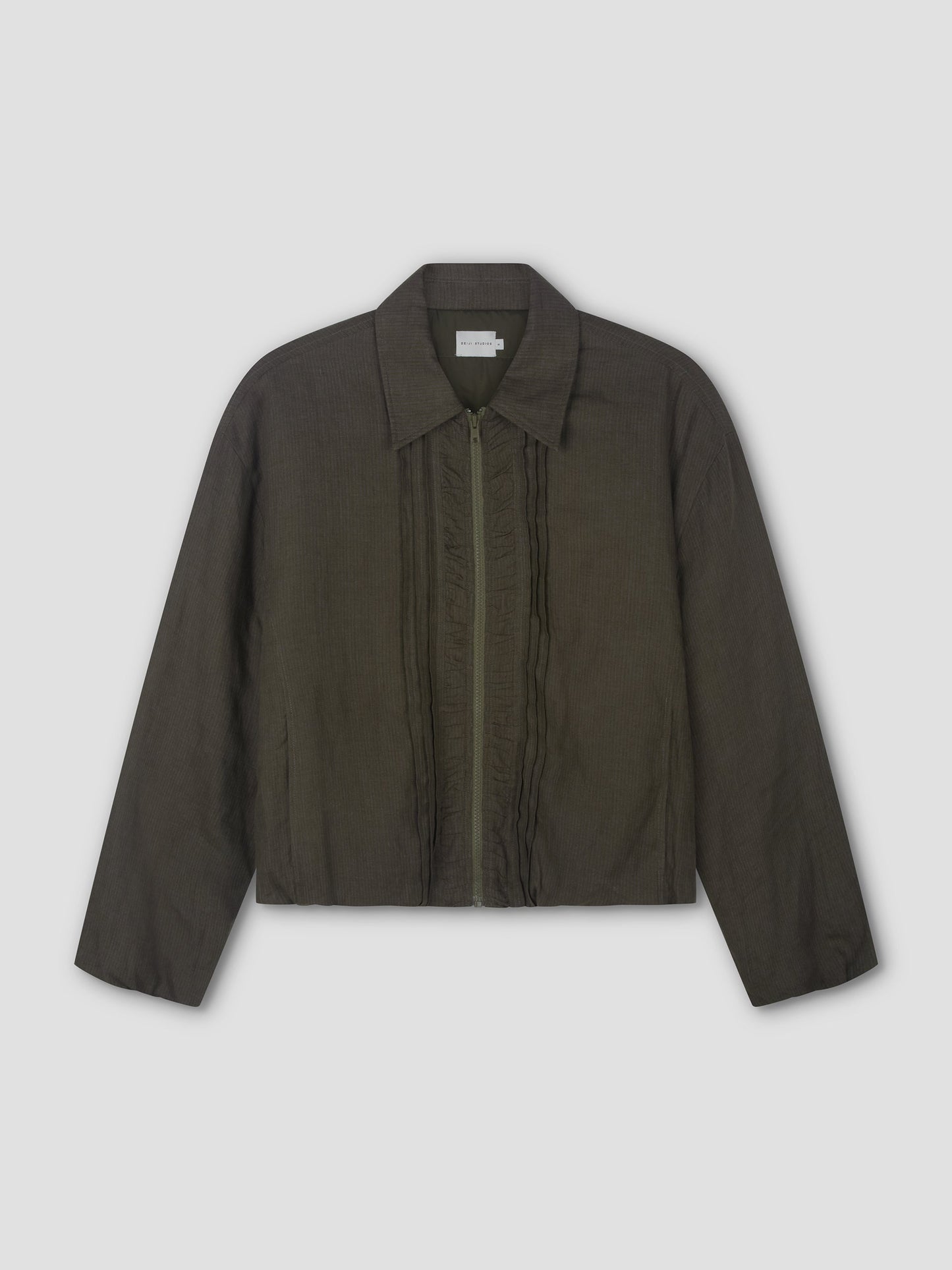 The Pintuck Jacket - Khaki Stripe by Deiji Studios is a dark olive green, long-sleeved bomber with a classic collar, front zip, subtle vertical ruffle details beside the zipper, and a straight hem. Shown laid flat on a light background.