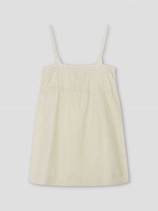 A sleeveless Edge Dress - Citrus Stripe by Deiji Studios, featuring a light yellow hue with thin spaghetti straps, gathered fabric at the chest, and a loose fit, shown against a plain light grey background.