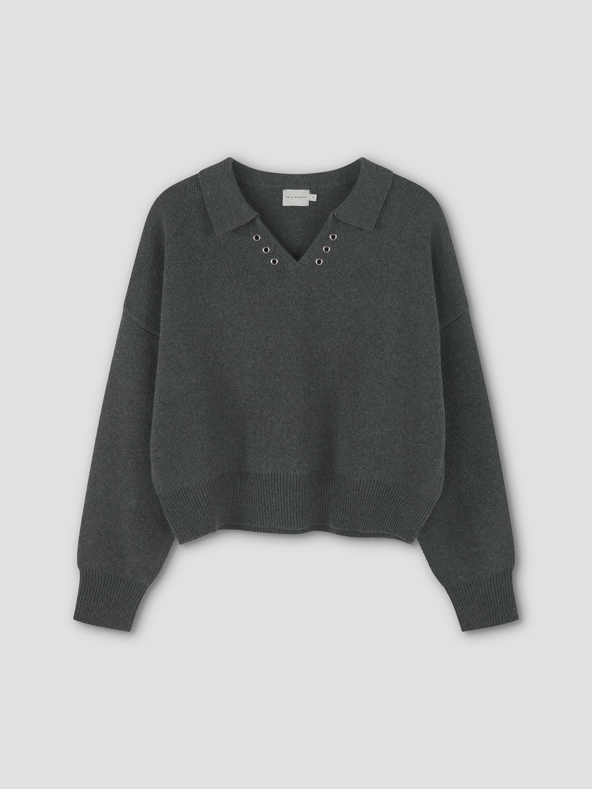 The Eyelet Knit - Dark Pebble by Deiji Studios is a dark gray relaxed long-sleeve sweater with a collar, V-neckline, and metal eyelets around the neck, shown laid flat on a plain light background.