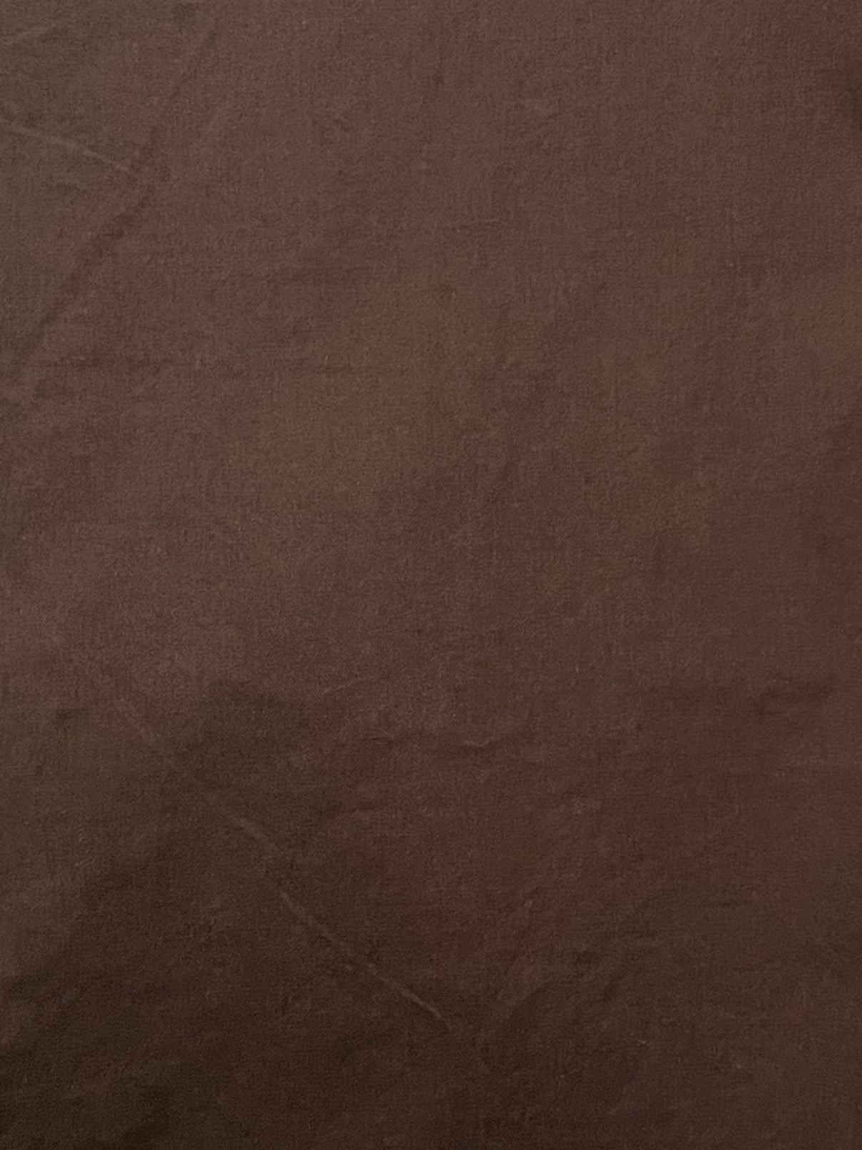 A close-up of the Turn Pant - Cocoa displays its brown organic cotton surface with subtle wrinkles and creases, highlighting a soft, smooth texture and even coloration.