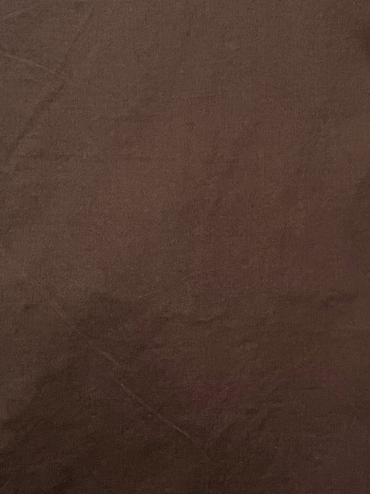 A close-up of the Turn Pant - Cocoa displays its brown organic cotton surface with subtle wrinkles and creases, highlighting a soft, smooth texture and even coloration.