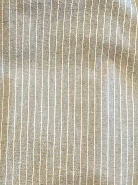 A close-up of the Long Lounger - Pistachio Stripe shows light gray organic cotton with thin white pinstripes, slight wrinkles, and a textured look—ideal for relaxing in comfort.