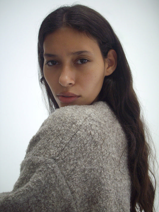 A person with long brown hair wearing the Pod Knit in Cloud Grey by Deiji Studios looks over their shoulder at the camera against a plain white background.