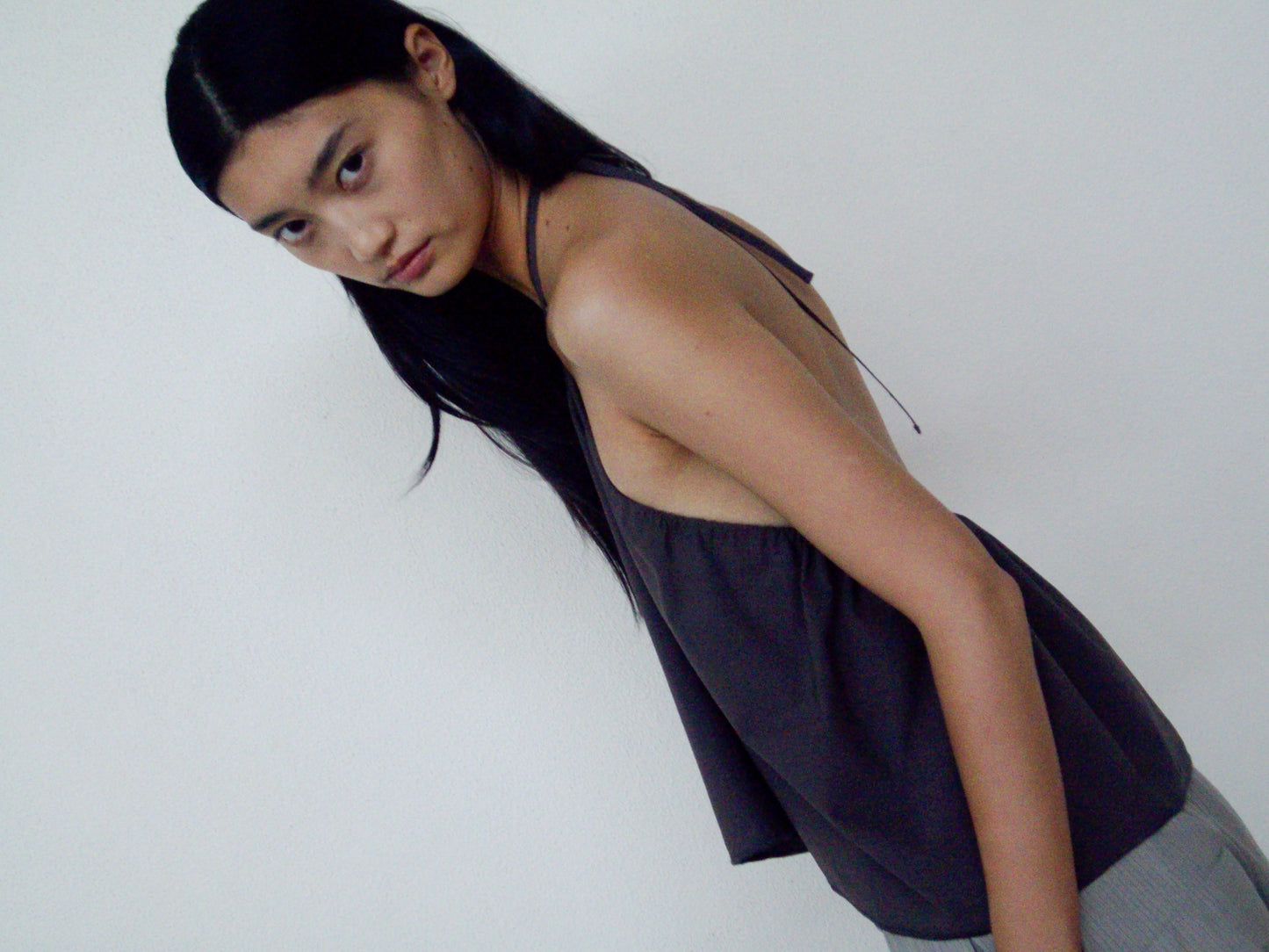 A person with long black hair wears the 0 Napkin Top in Chocolate—an organic cotton, loose-fitting top—while standing against a plain white wall and looking seriously at the camera.