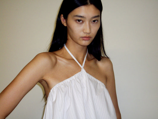 A person with long dark hair wears the Napkin Top - Pacific Stripe by 0, standing against a light background and looking directly at the camera with a neutral expression.