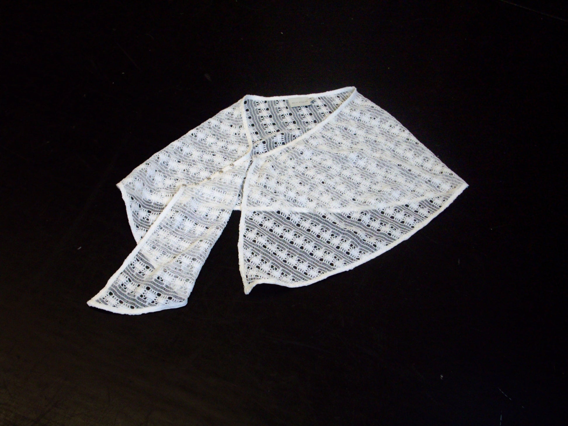 The Thread Button Belt in off white is displayed flat on a black surface, with one end folded over the other.