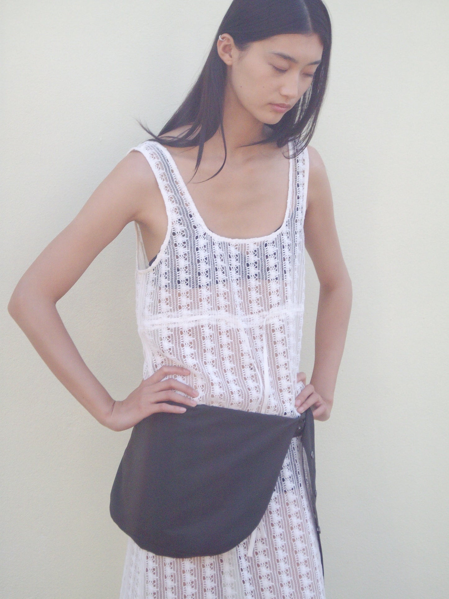 A woman with long dark hair wears the Thread Dress - Off White by 0 and a large black belt bag, posing with hands on hips against a plain light-colored background.