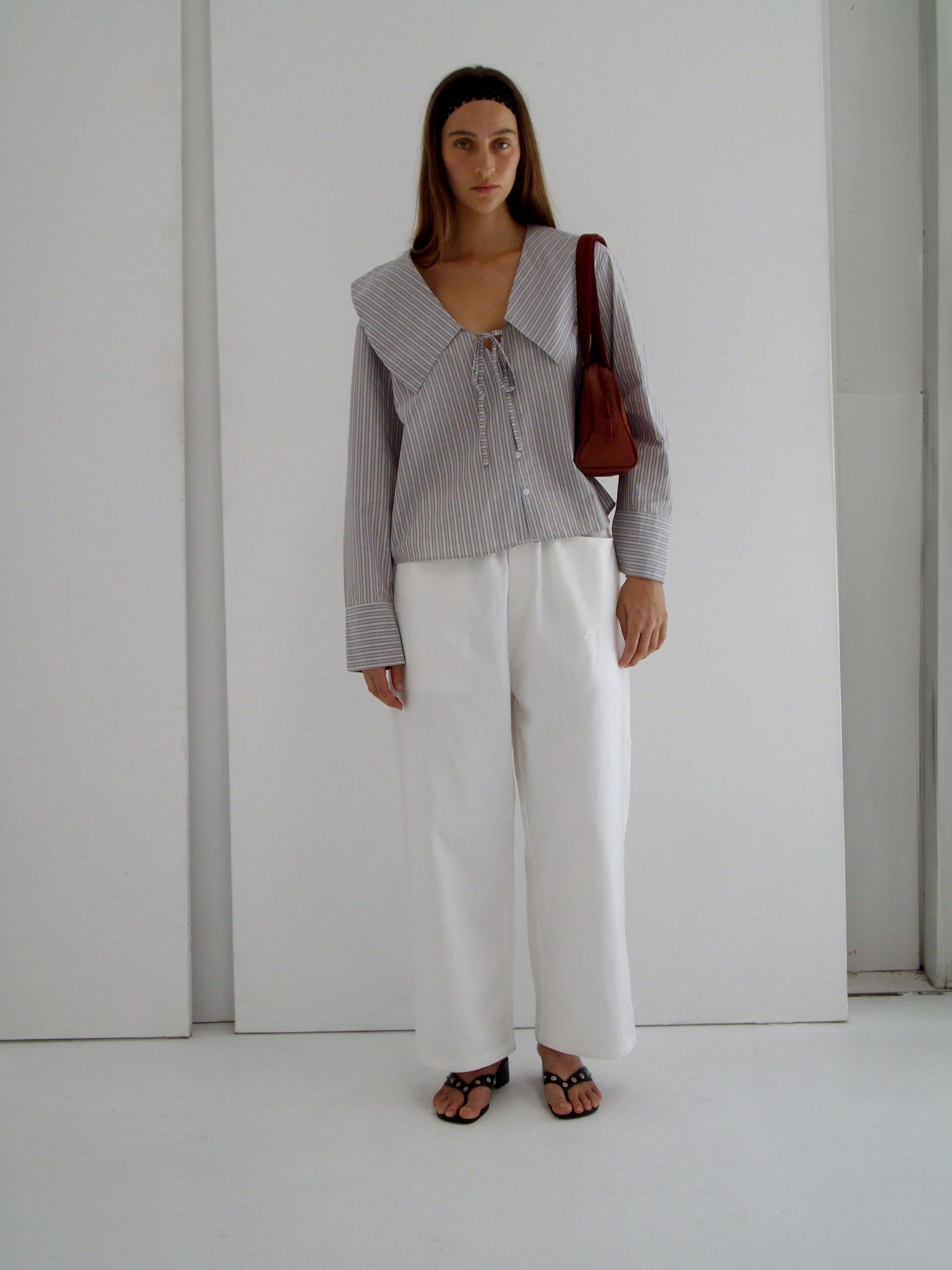 female model wears the collared tie shirt by Deiji Studios in seas stripe


a structured shirt features an oversized collar and cuff, tie at front collar opening, dropped shoulder and elongated sleeves in a boxy fit


made from 100% GOTS certified organic cotton poplin

paired with a white cotton trouser