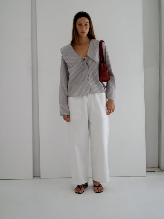 female model wears the collared tie shirt by Deiji Studios in seas stripe


a structured shirt features an oversized collar and cuff, tie at front collar opening, dropped shoulder and elongated sleeves in a boxy fit


made from 100% GOTS certified organic cotton poplin

paired with a white cotton trouser