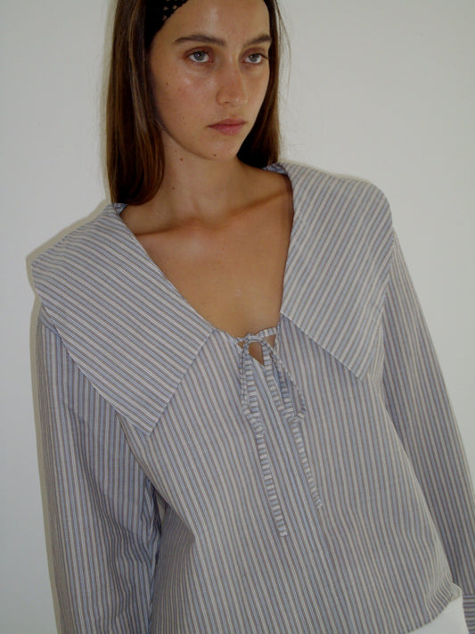 female model wears the collared tie shirt by Deiji Studios in seas stripe


a structured shirt features an oversized collar and cuff, tie at front collar opening, dropped shoulder and elongated sleeves in a boxy fit


made from 100% GOTS certified organic cotton poplin