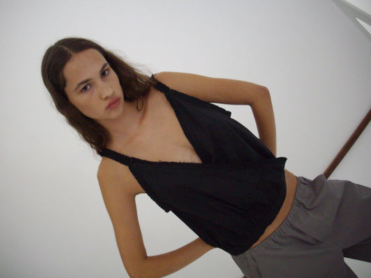 A person with long brown hair wears a sleeveless black top and the Curve Pant - Lavender Smoke, featuring a relaxed fit and mid-rise waist, standing hands on hips against a plain white background, looking directly at the camera with a neutral expression.