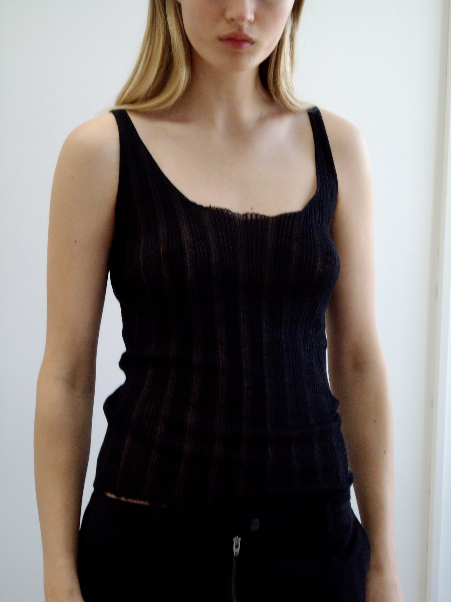 A woman with long blonde hair wears the Deiji Studios Open Work Tank in black and matching pants, standing against a light plain background with her face partially out of frame.