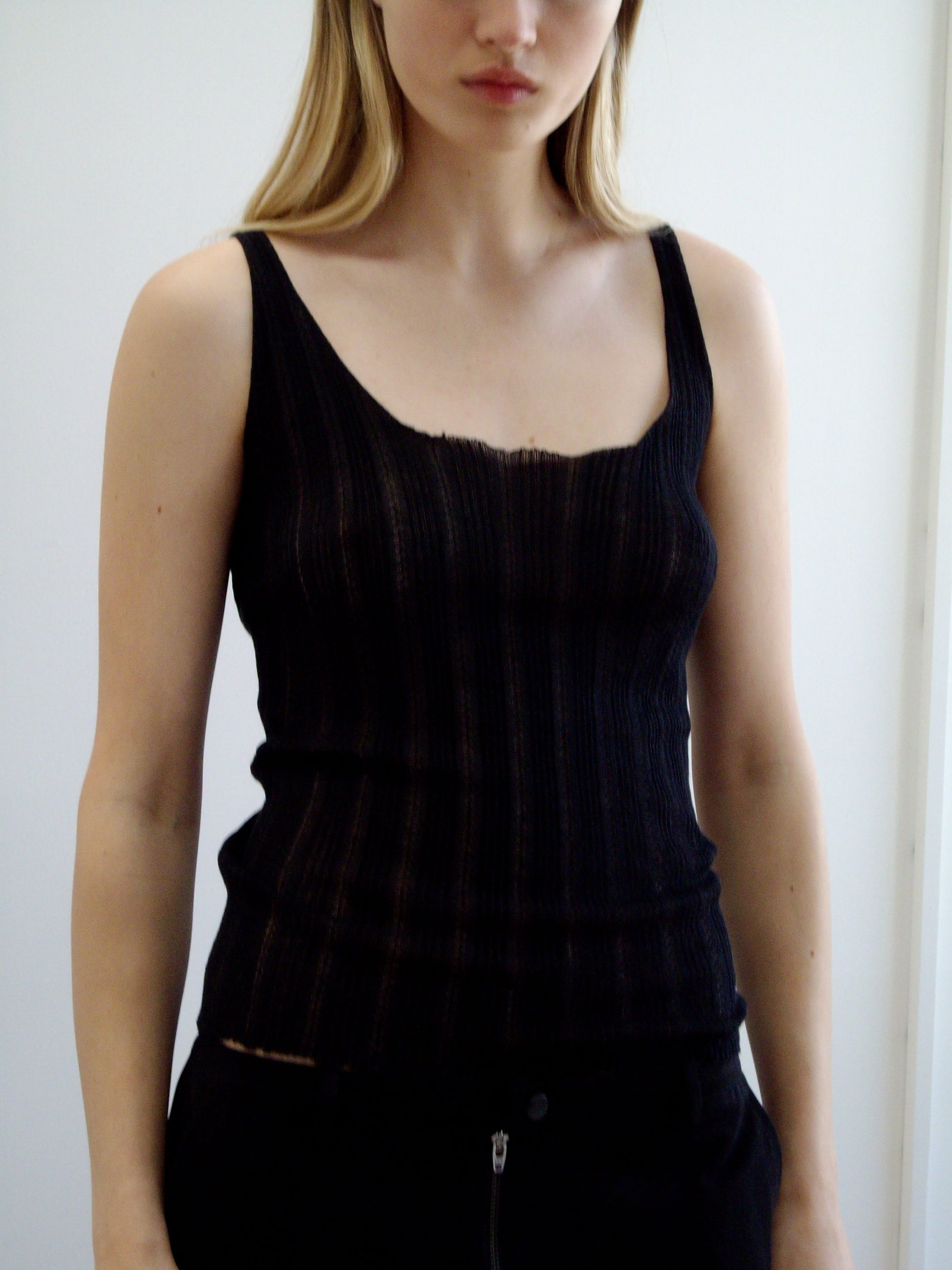 A woman with long blonde hair wears the Deiji Studios Open Work Tank in black and matching pants, standing against a light plain background with her face partially out of frame.