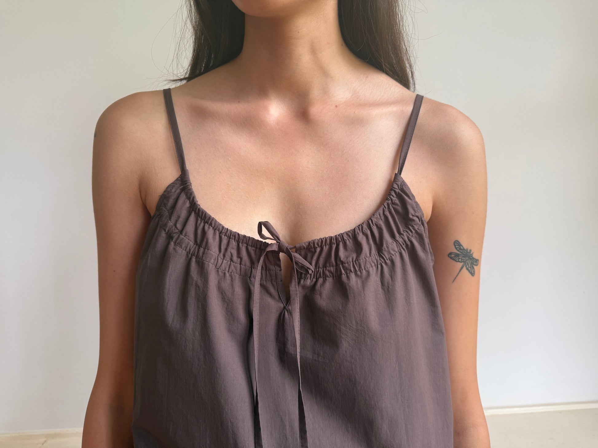 A woman with long hair and a dragonfly tattoo on her upper arm wears the Light Dress - Chocolate by 0, posing against a plain light background. Her face is partially out of frame.