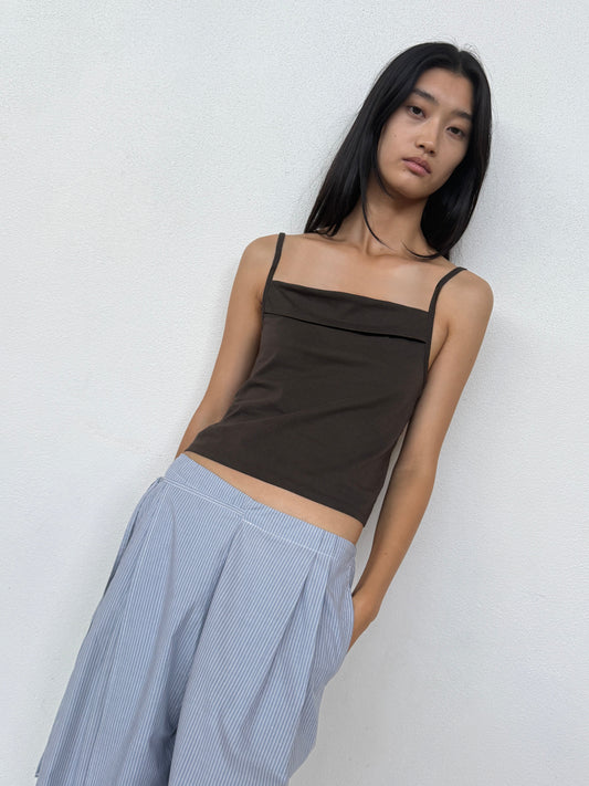 A person with long dark hair wears the 0 Double Layer Pant - Sky Stripe and a sleeveless brown top, standing against a plain white wall and looking at the camera.