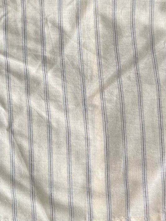 A close-up of the Ruffle Button Top - Raquette Stripe by Deiji Studios, showing light beige organic cotton with evenly spaced vertical blue stripes and subtle wrinkles in the fabric.