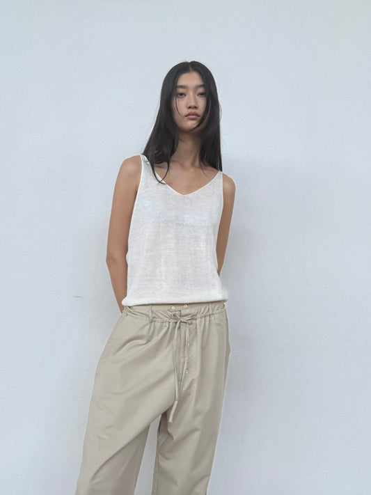 A woman with long black hair wears the 0 Rolled Knit Top in Off White, standing against a plain light gray wall and looking directly at the camera with a neutral expression.