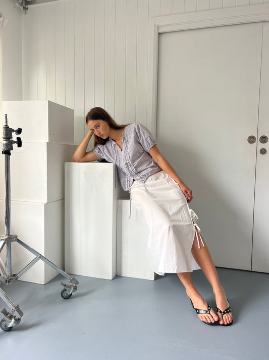 female model wears the double frill top by Deiji Studios in seas stripe



elevated everyday top features a flattering v neckline with button down front, fixed ruffle details, soft blouson sleeve and gathered elastic cuffs


made from 100% GOTS certified organic cotton poplin

paired with a white skirt