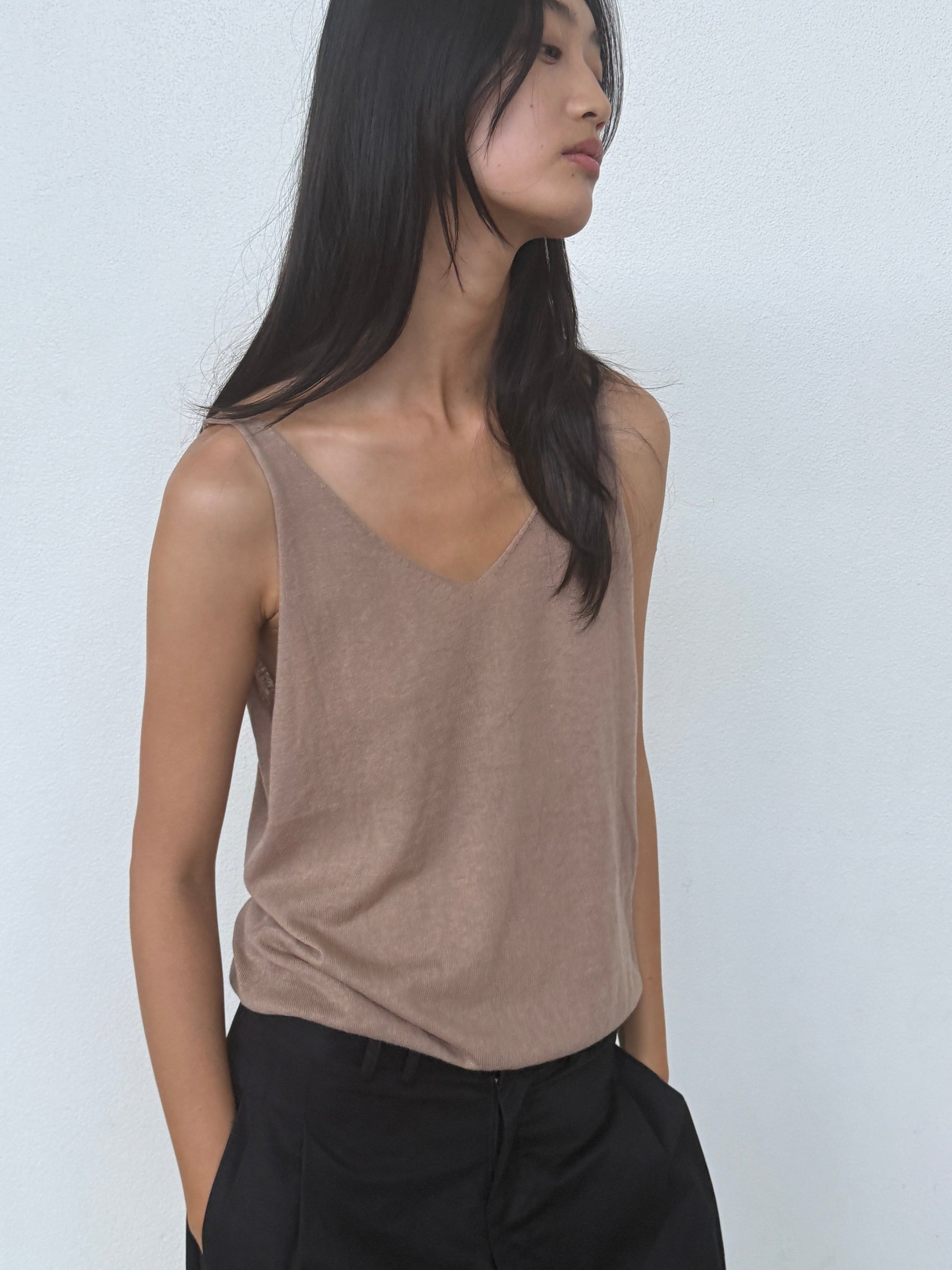 A person with long black hair wears the 0 Rolled Knit Top in Light Brown and black pants, standing against a plain white background and looking to the side with hands in their pockets.