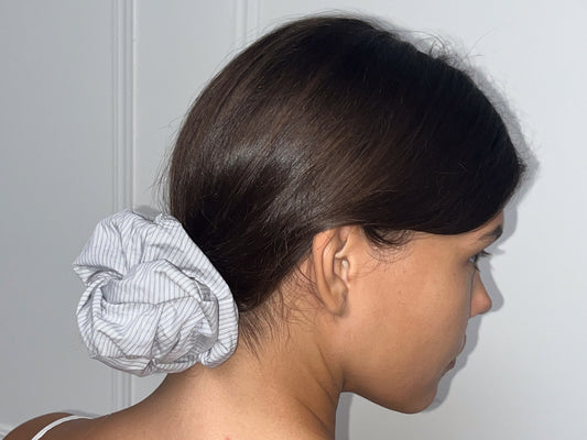 A person with straight brown hair in a low bun, secured with the Scrunchie, is shown from the side against a white background.