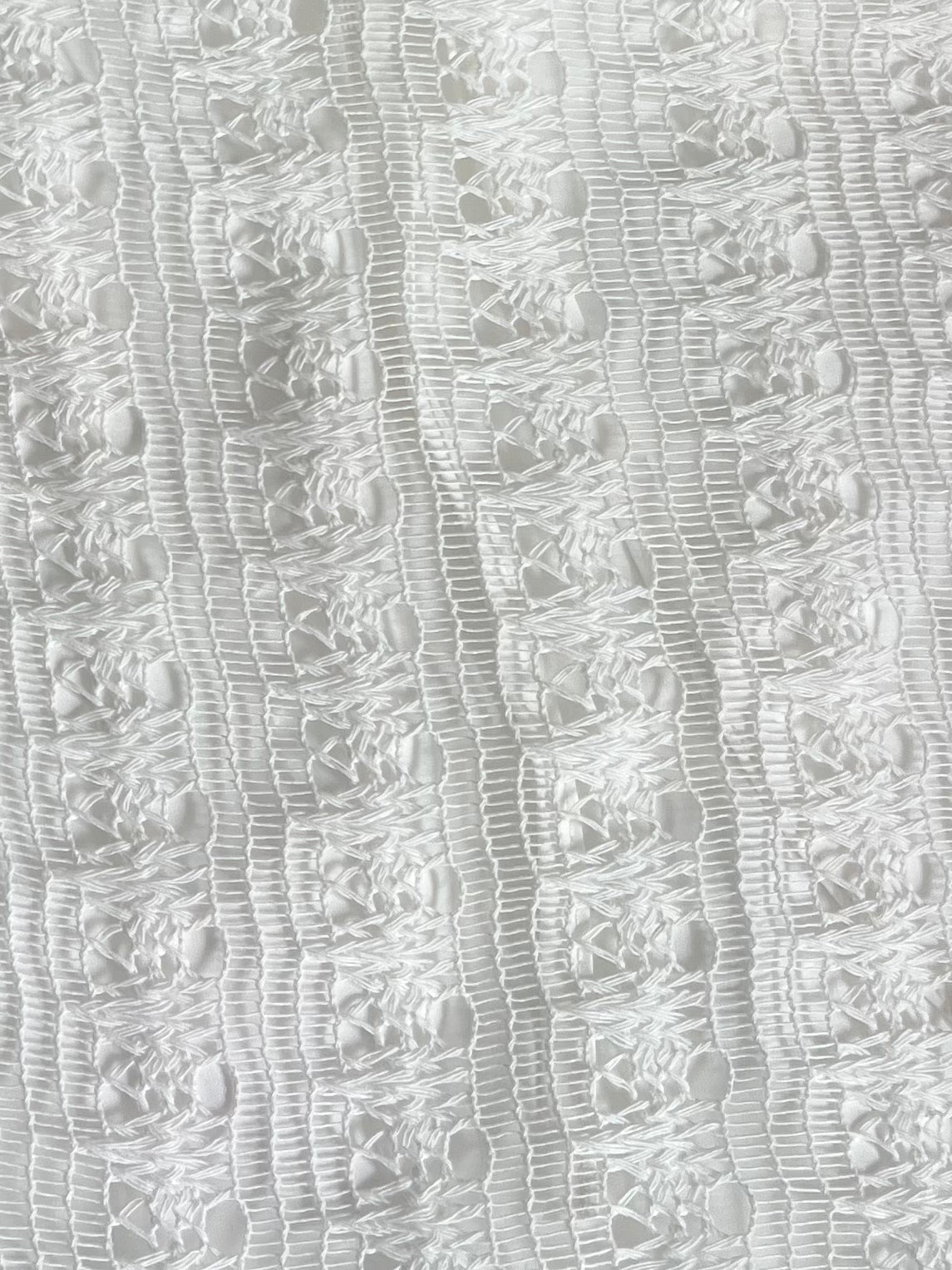 Close-up of the Thread Button Belt in Off White, made from organic cotton with textured lace featuring vertical lines and geometric openwork. The delicate material appears airy with a subtle sheen.