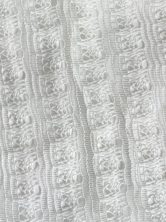 Close-up of the Thread Button Belt in Off White, made from organic cotton with textured lace featuring vertical lines and geometric openwork. The delicate material appears airy with a subtle sheen.