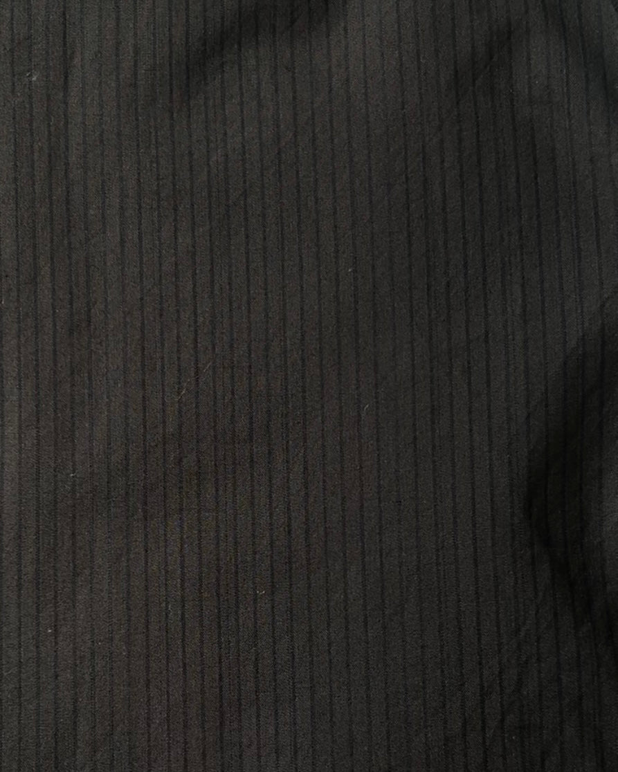 Close-up of the Layered Short - Black Stripe by 0, featuring smooth dark black fabric with subtle vertical pinstripes, crafted from organic cotton and showing soft folds.