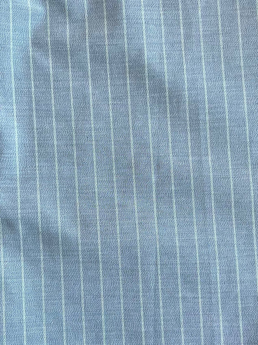Close-up of light blue Tri Pleat Pure Wool Pant - Steele Stripe by Deiji Studios, featuring RWS wool fabric with thin white vertical pinstripes and subtle wrinkles.